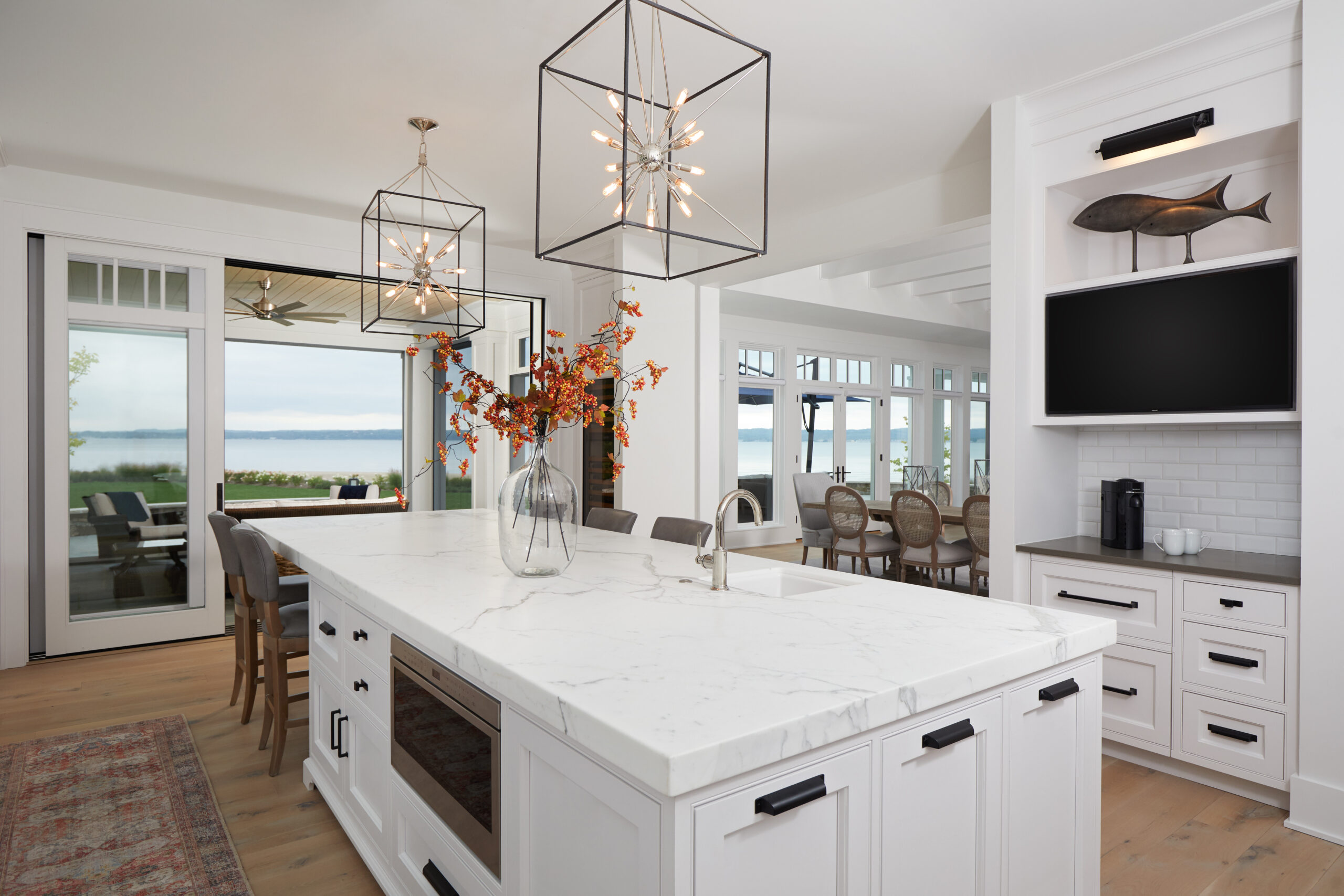 Modern coastal kitchen with white cabinetry, marble island, and lake views.