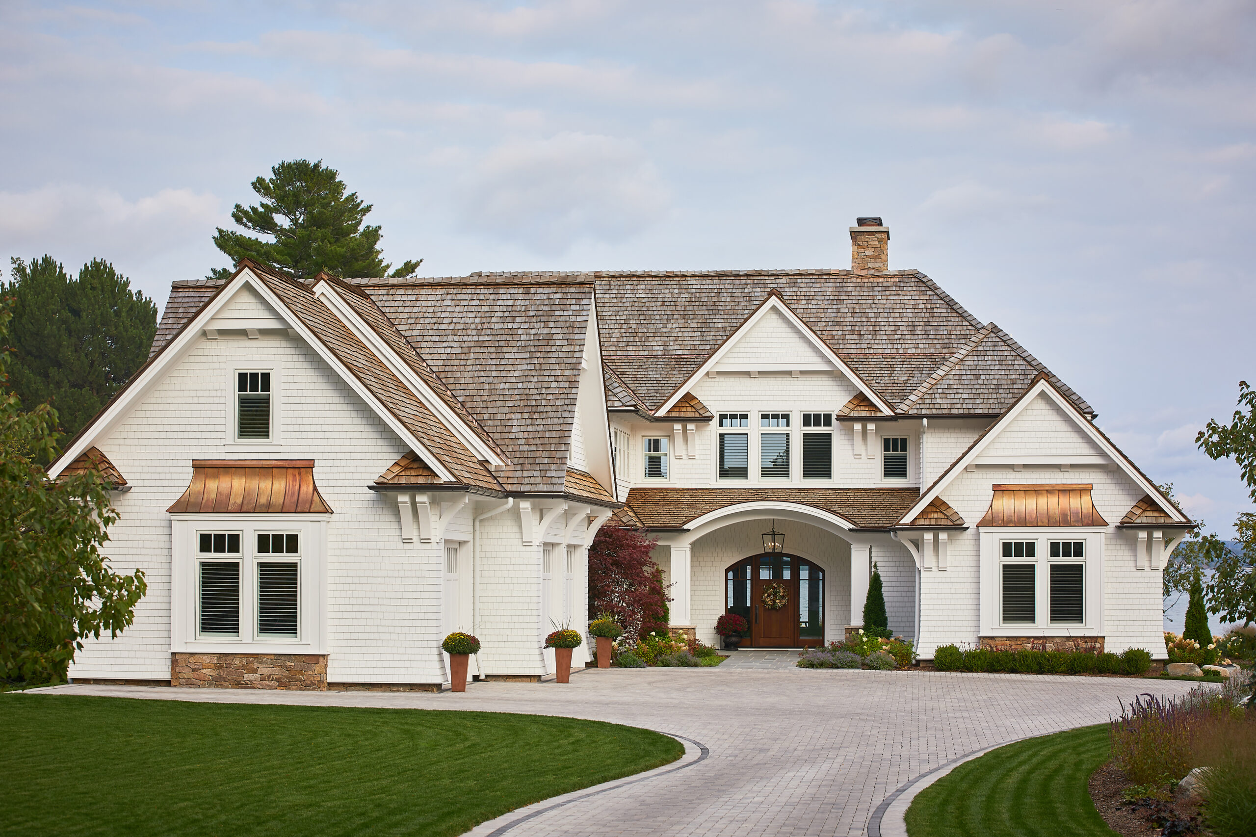 Front view of a white luxury home with cedar roof and curved driveway.