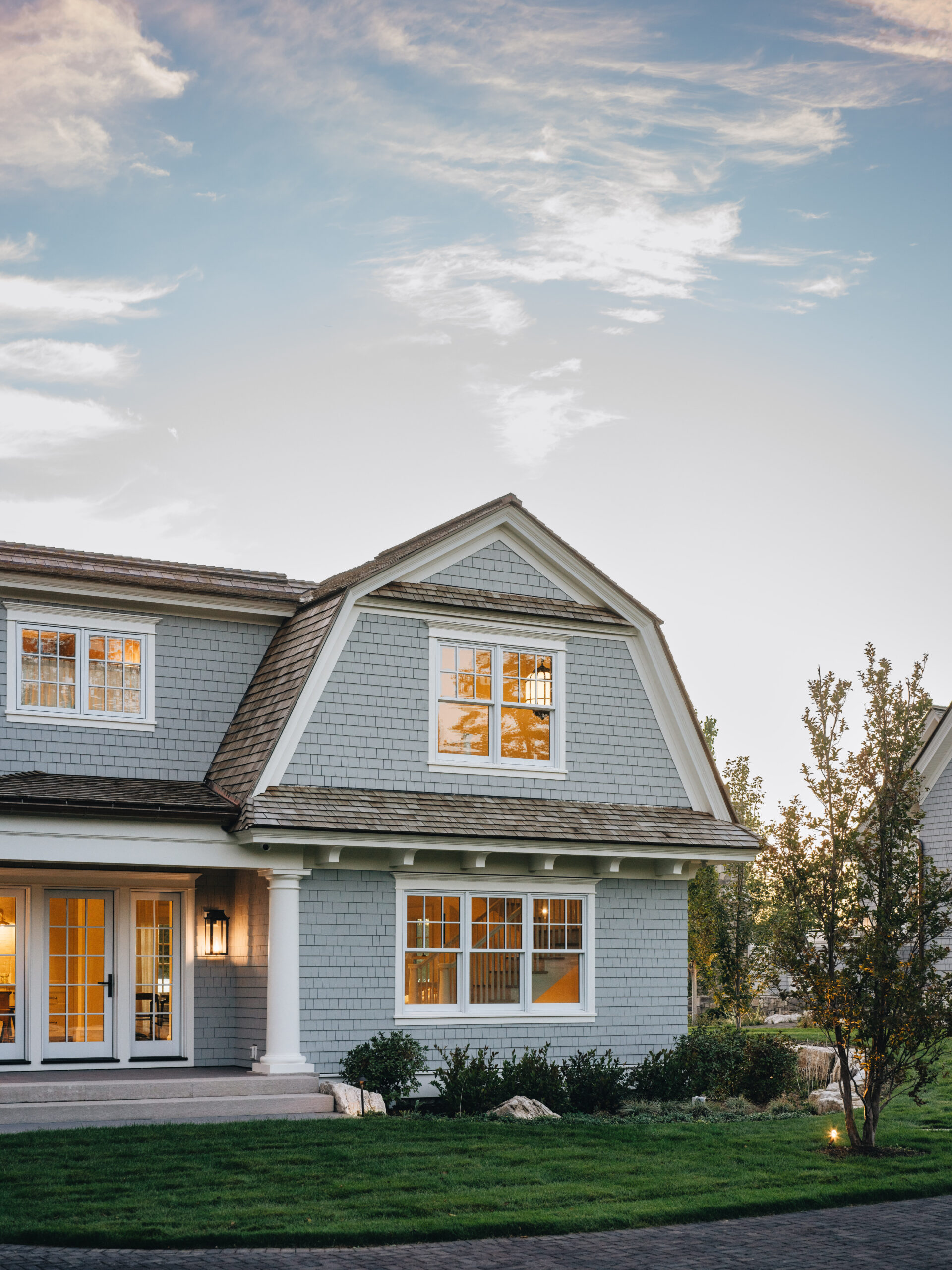 Front exterior of Glen Lake guest house at sunset with shake siding, dormer window, and glowing interior lights