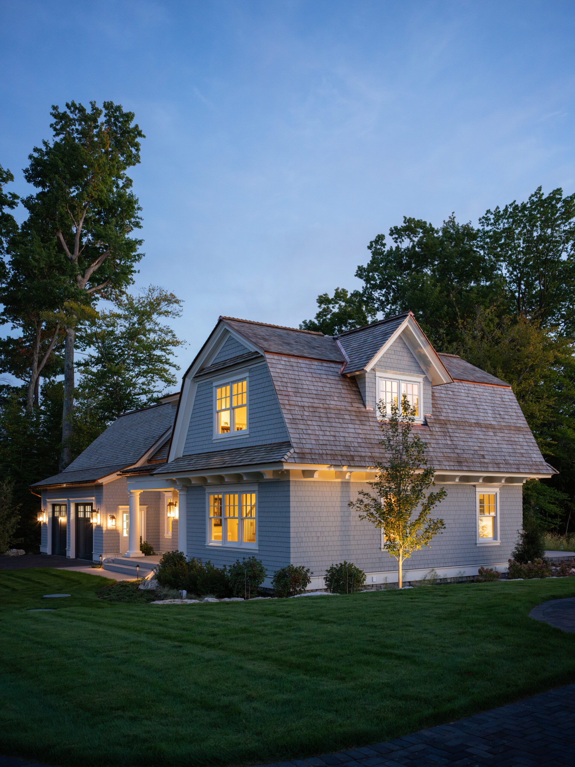 Guest house exterior at dusk with cedar shake siding, warm interior lighting, and manicured lawn.