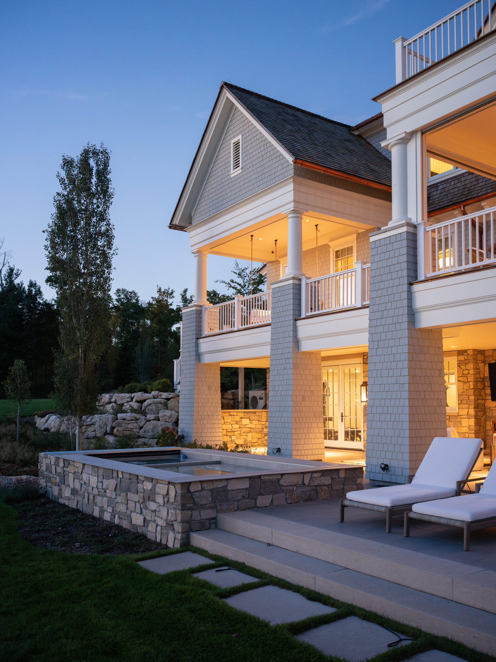 Twilight exterior of Glen Lake custom home with stone patio, spa, and upper-level porches