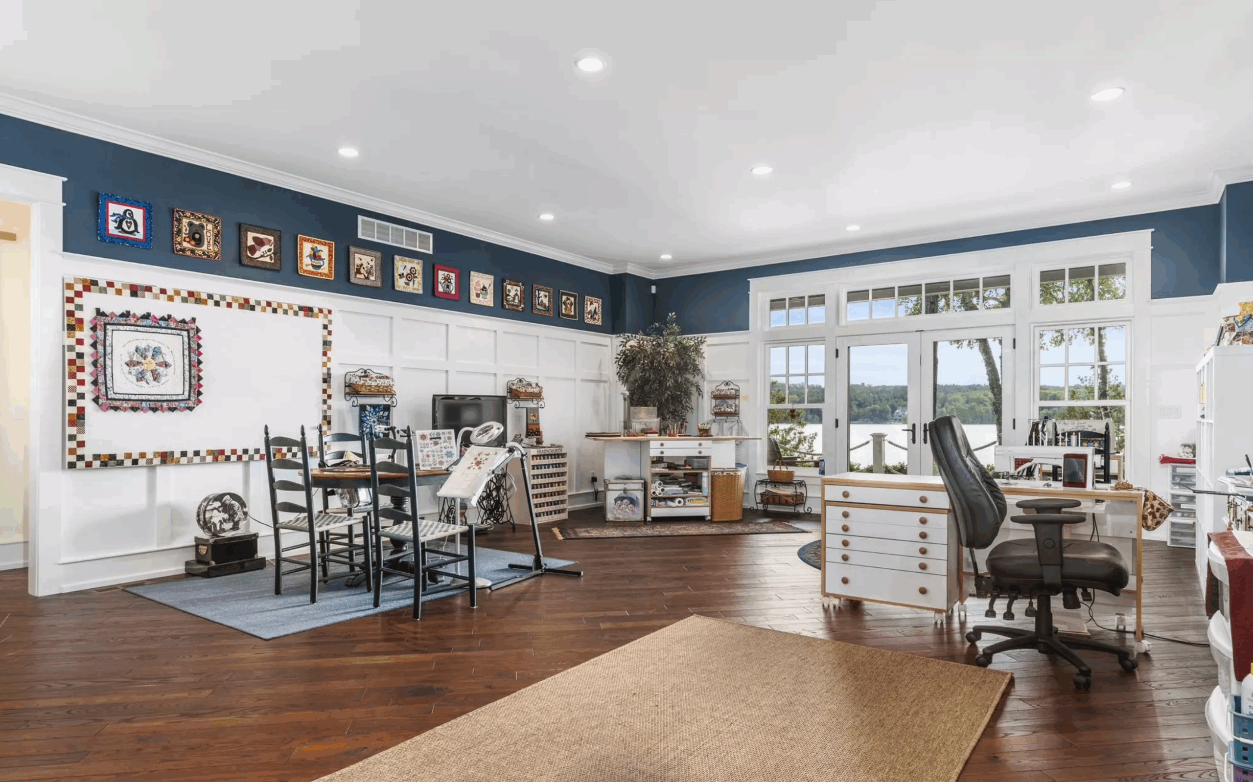 Bright craft and sewing studio with blue walls, white wainscoting, worktables, and lake-view French doors