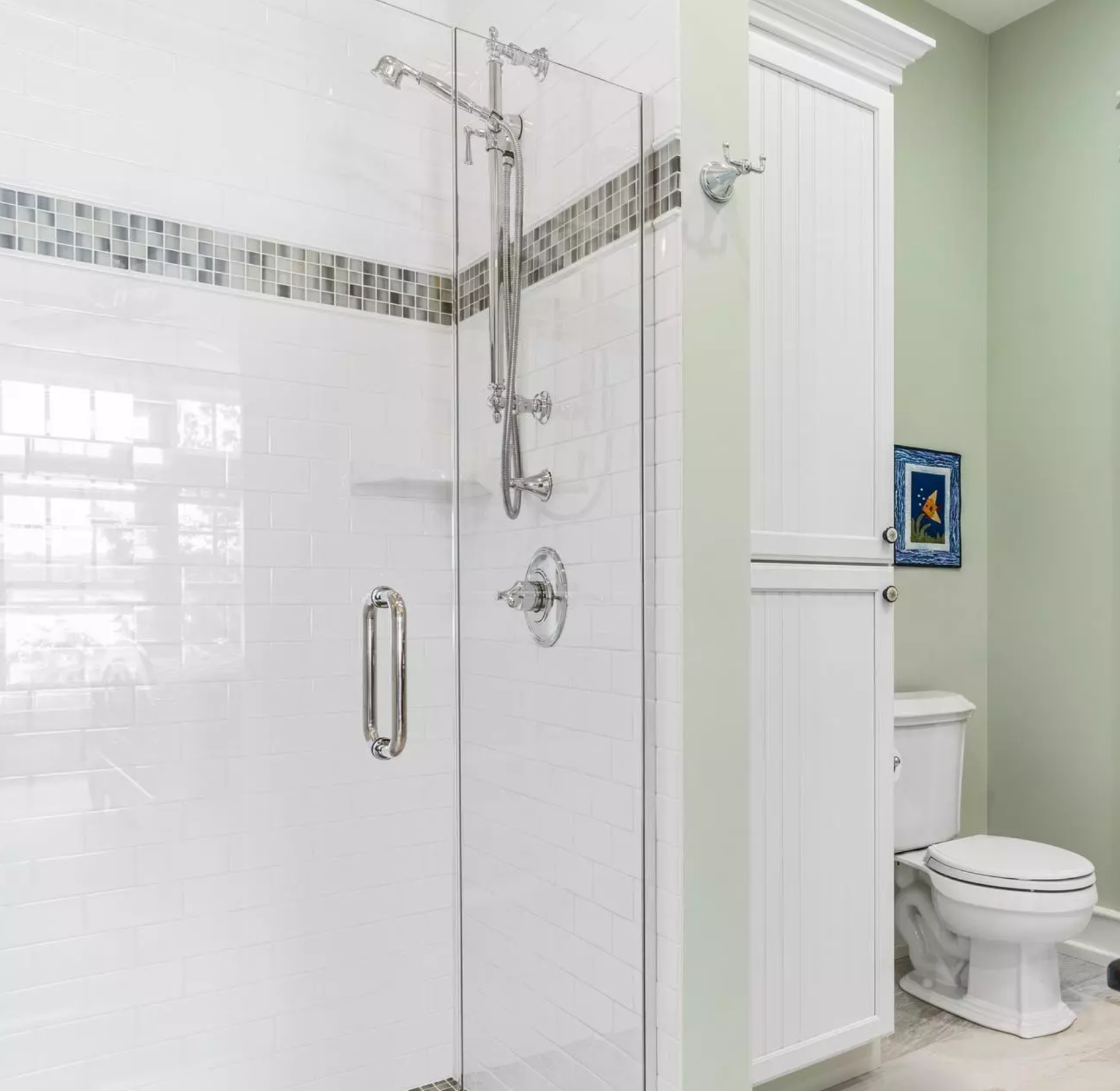 Glass-enclosed shower with white subway tile, mosaic accent band, and chrome fixtures in a light green bathroom